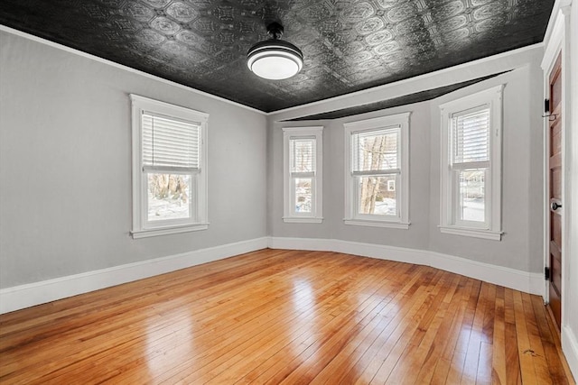 empty room with an ornate ceiling, a wealth of natural light, hardwood / wood-style floors, and baseboards