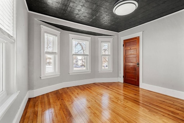 empty room featuring ornamental molding, hardwood / wood-style flooring, an ornate ceiling, and baseboards