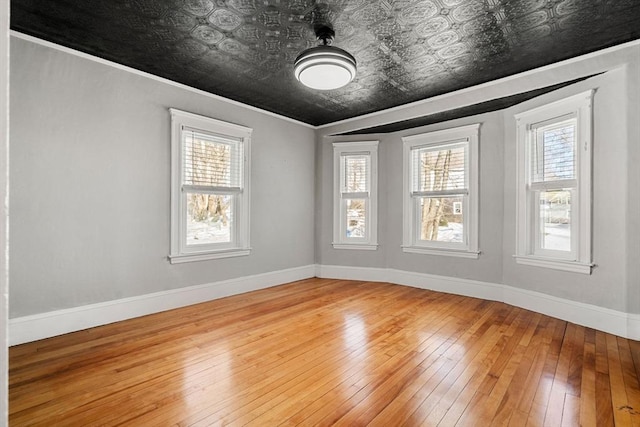 empty room with hardwood / wood-style flooring, an ornate ceiling, baseboards, and ornamental molding