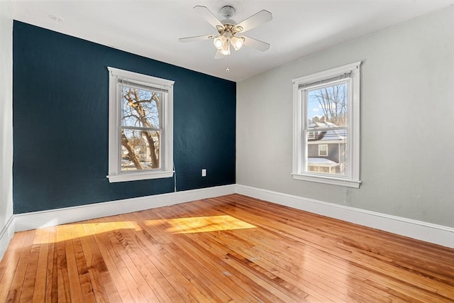 spare room with baseboards, a ceiling fan, hardwood / wood-style flooring, and a healthy amount of sunlight