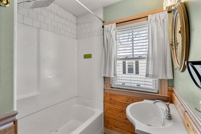 bathroom with a wainscoted wall, a sink, wooden walls, and shower / tub combination