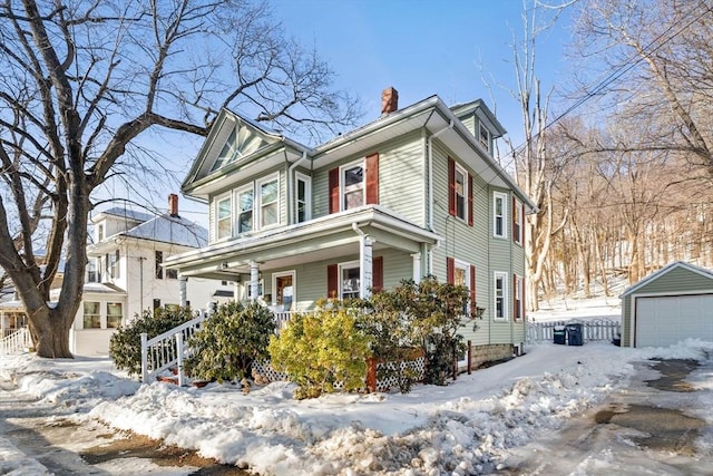 view of front of house with an outbuilding, covered porch, a detached garage, and a chimney