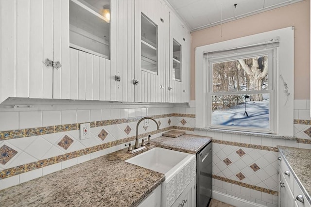 kitchen with a sink, tile walls, white cabinetry, stainless steel dishwasher, and glass insert cabinets