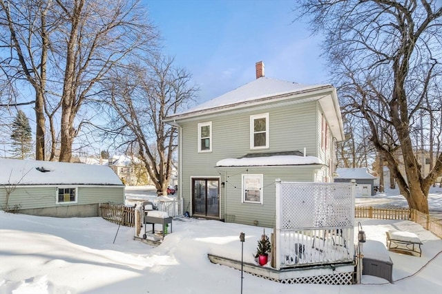 snow covered rear of property with a chimney and fence