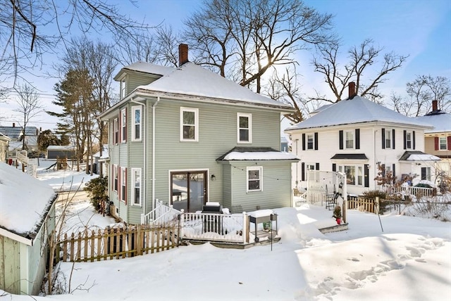 snow covered back of property featuring a chimney and fence