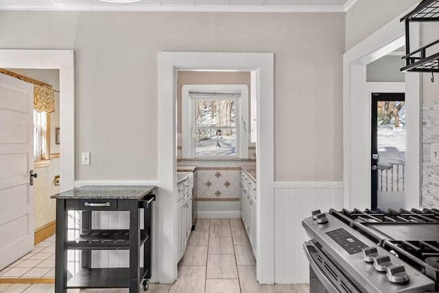 kitchen featuring a wainscoted wall, plenty of natural light, white cabinetry, and stainless steel range with gas stovetop