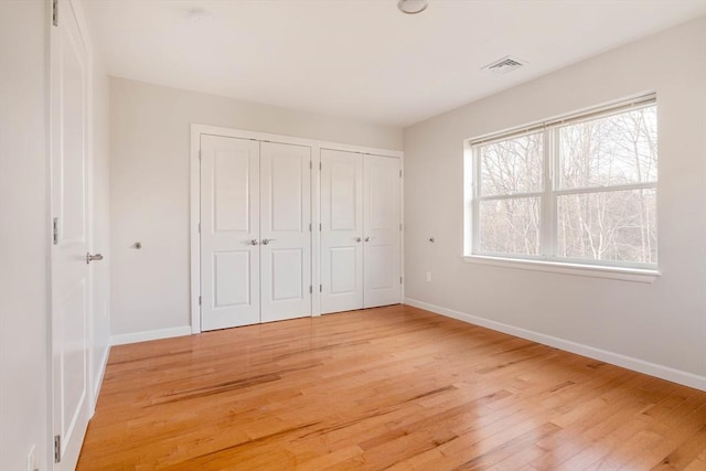 unfurnished bedroom with visible vents, baseboards, two closets, and light wood finished floors