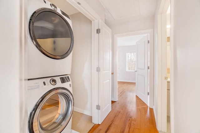 washroom featuring laundry area, baseboards, stacked washer / drying machine, and light wood finished floors