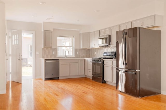 kitchen with light wood-style flooring, a sink, backsplash, appliances with stainless steel finishes, and light countertops