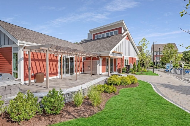 back of property with a lawn, board and batten siding, a pergola, and roof with shingles