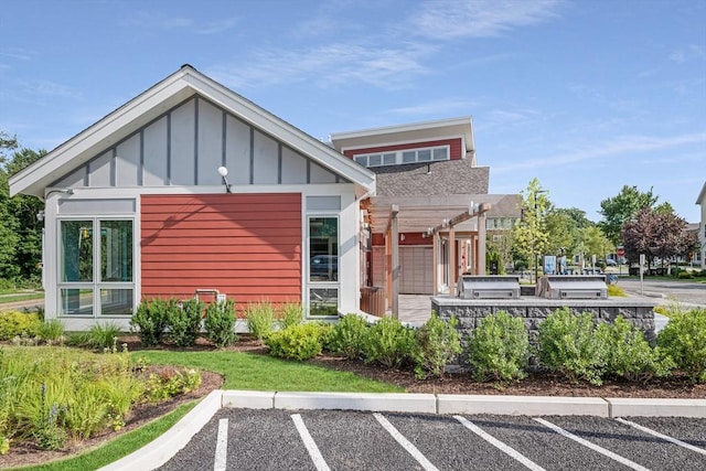 rear view of house with board and batten siding, uncovered parking, and a pergola