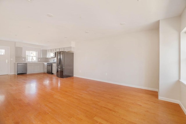 unfurnished living room featuring light wood-style flooring, baseboards, and a sink