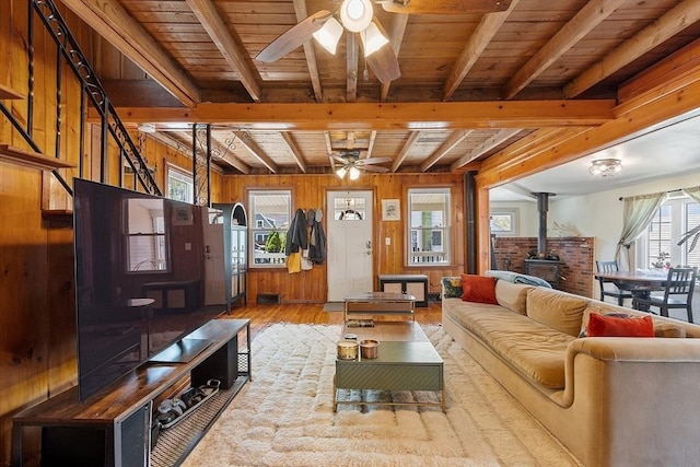 living room featuring a wood stove, a ceiling fan, beamed ceiling, and hardwood / wood-style flooring
