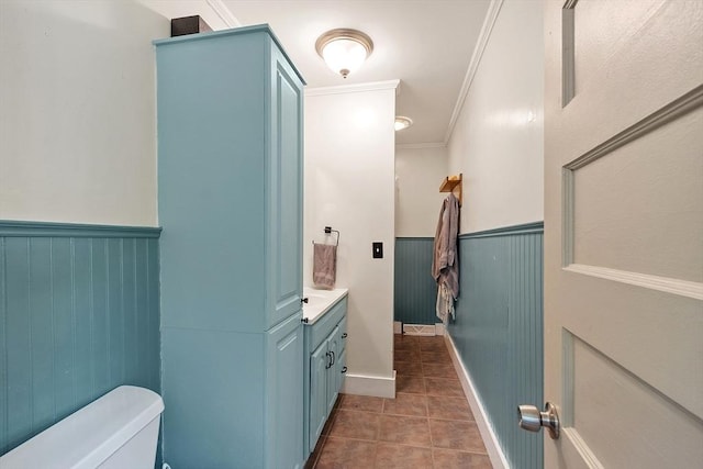 half bath with toilet, tile patterned flooring, wainscoting, vanity, and ornamental molding