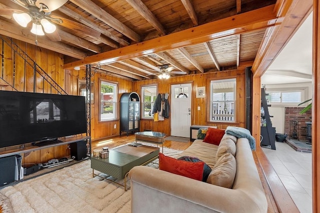 living area featuring beamed ceiling, wooden walls, ceiling fan, and a wealth of natural light