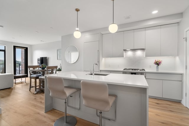 kitchen featuring a kitchen island with sink, light hardwood / wood-style flooring, decorative light fixtures, sink, and white cabinets