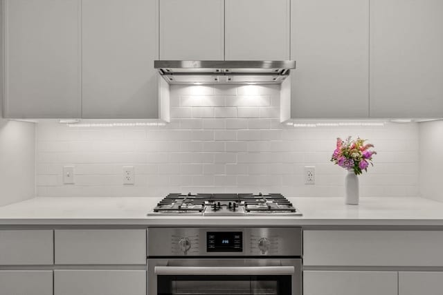 kitchen with under cabinet range hood, light countertops, appliances with stainless steel finishes, backsplash, and modern cabinets