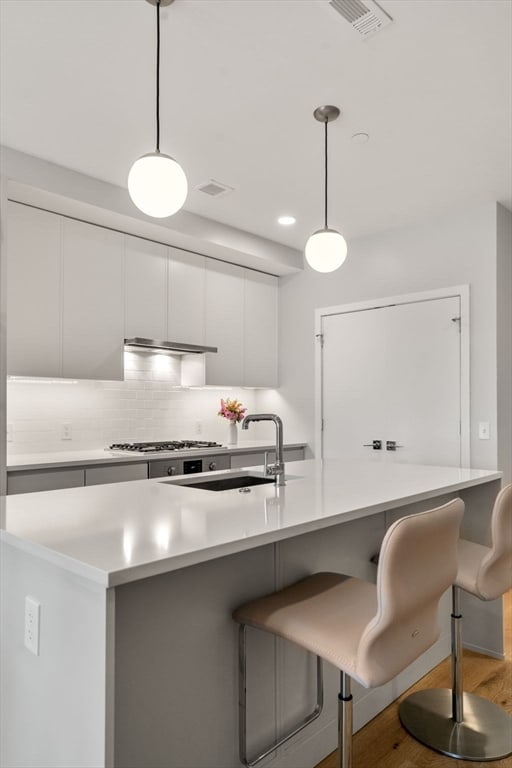 kitchen featuring backsplash, a kitchen breakfast bar, wood-type flooring, hanging light fixtures, and white cabinets