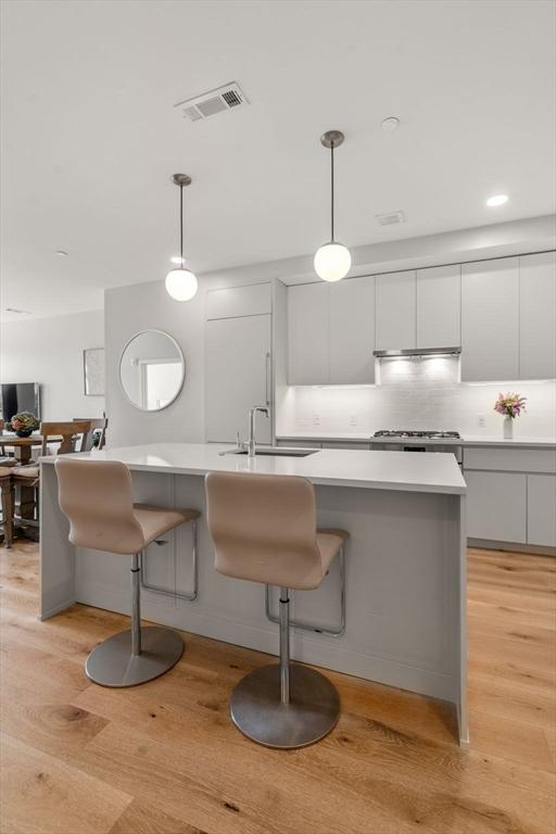 kitchen featuring visible vents, white cabinets, light wood-style flooring, light countertops, and a sink