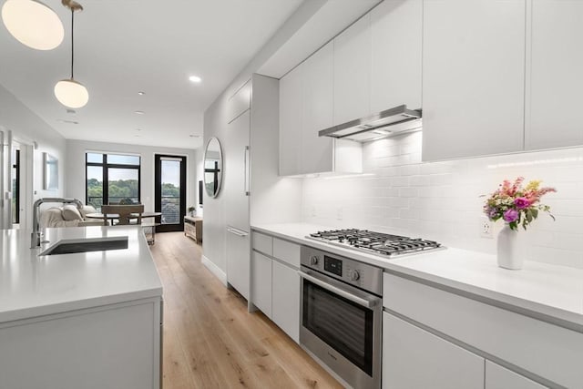 kitchen with light countertops, appliances with stainless steel finishes, open floor plan, a sink, and under cabinet range hood