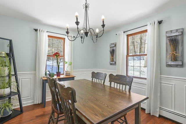 dining room with dark wood-style floors, a baseboard radiator, a wainscoted wall, and a notable chandelier