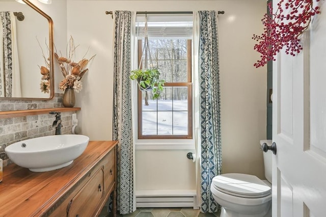 half bathroom featuring a baseboard heating unit, vanity, toilet, and decorative backsplash