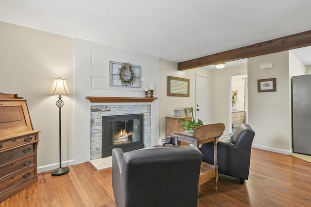 living area featuring a brick fireplace, wood finished floors, beam ceiling, and baseboards