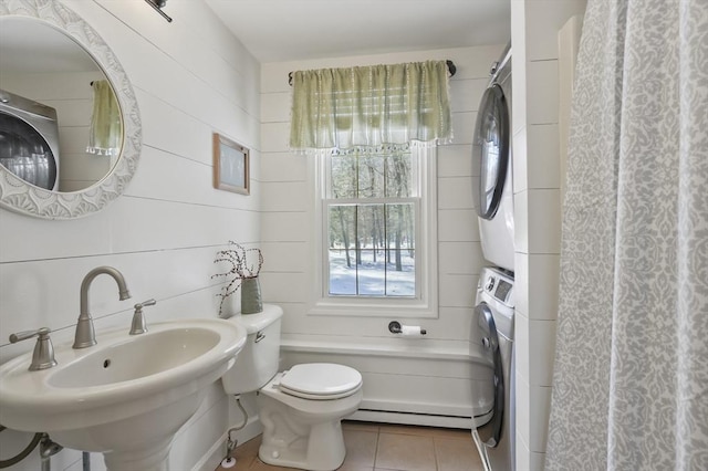 full bathroom with a baseboard radiator, tile patterned flooring, toilet, stacked washer / dryer, and a sink