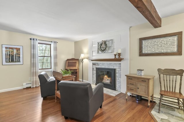 living room featuring dark wood-style flooring, beam ceiling, a baseboard heating unit, a brick fireplace, and baseboards