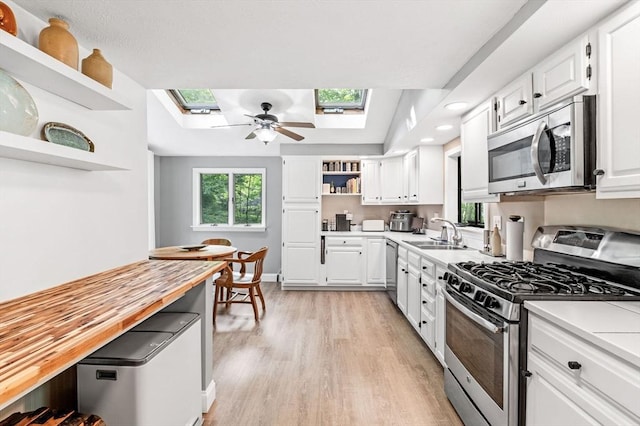 17 High St, Merrimac, MA 01860 - kitchen with open shelves, stainless steel appliances, a skylight, light wood-type flooring, and white cabinetry