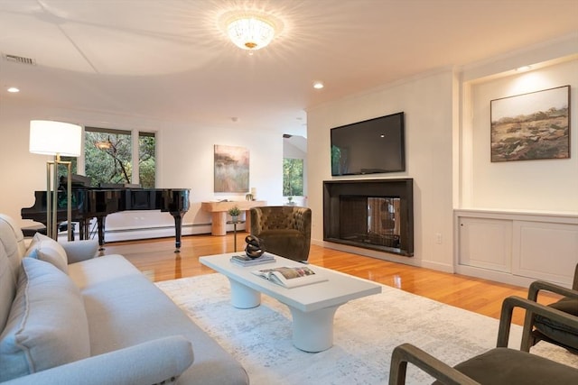 living room featuring light wood-type flooring, an inviting chandelier, a multi sided fireplace, and a baseboard radiator