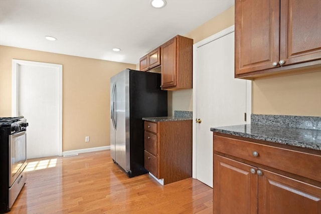 kitchen with light wood-style floors, brown cabinetry, stainless steel appliances, and dark stone countertops