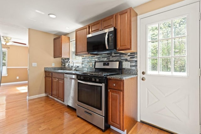 kitchen with appliances with stainless steel finishes, a sink, light wood-style flooring, baseboards, and backsplash