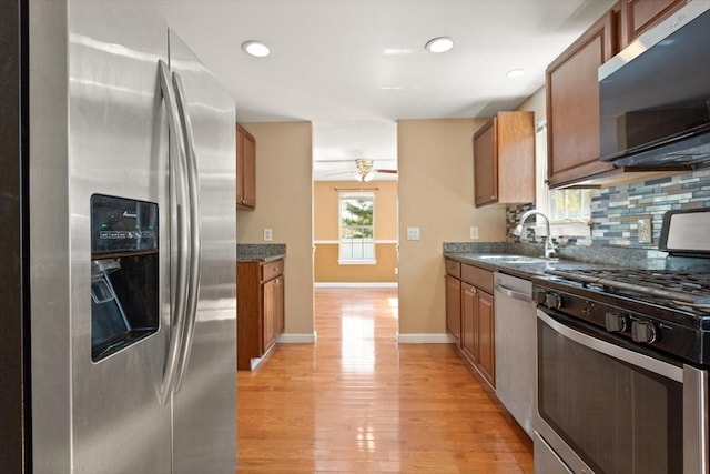 kitchen featuring a sink, brown cabinetry, light wood-style flooring, stainless steel appliances, and backsplash