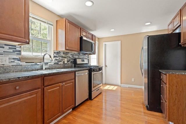 kitchen featuring decorative backsplash, light wood-type flooring, brown cabinets, a sink, and stainless steel appliances