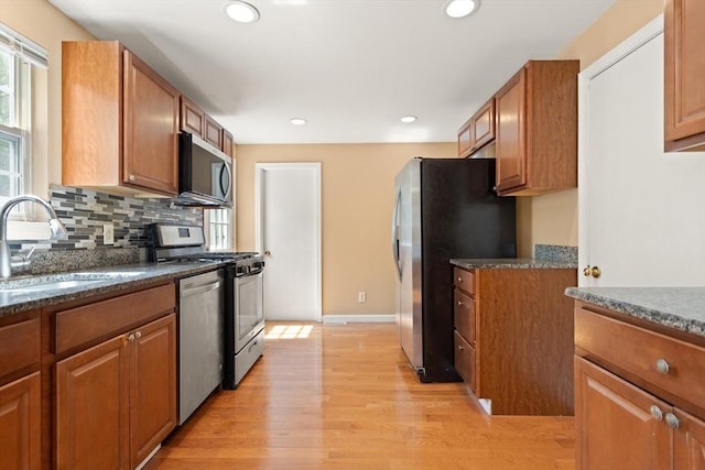 kitchen with appliances with stainless steel finishes, tasteful backsplash, brown cabinets, a sink, and light wood-style flooring