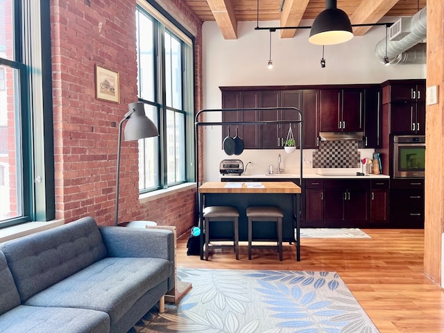 kitchen with beam ceiling, light hardwood / wood-style flooring, oven, wood ceiling, and brick wall