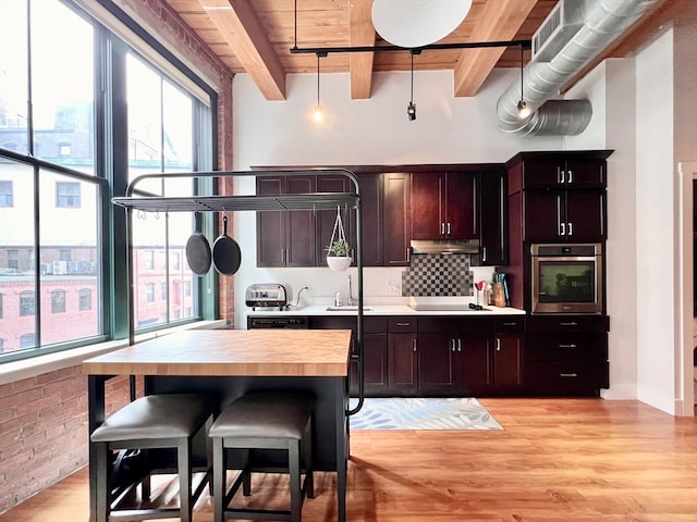 kitchen with stainless steel oven, hanging light fixtures, beam ceiling, and light wood-type flooring