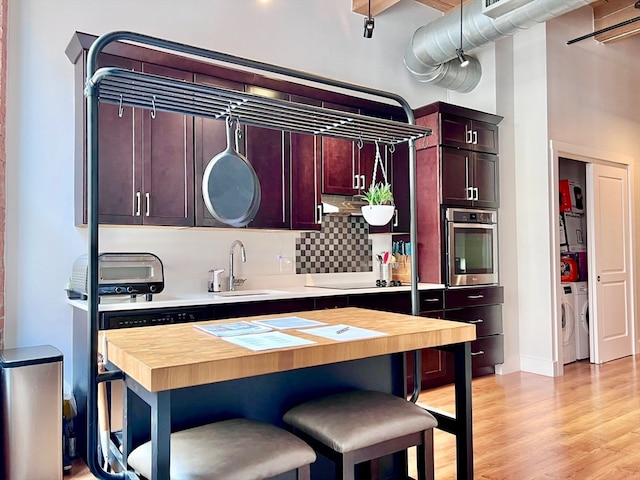 kitchen featuring washer and clothes dryer, tasteful backsplash, light hardwood / wood-style flooring, oven, and sink