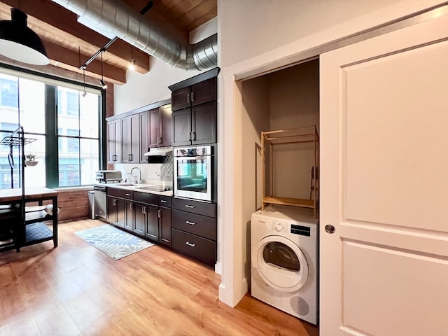 kitchen featuring light wood-type flooring, beam ceiling, dark brown cabinets, stainless steel oven, and washer / clothes dryer