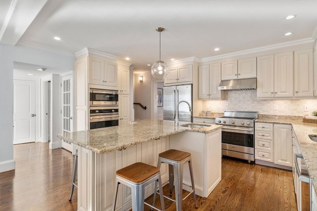 kitchen with pendant lighting, sink, a center island with sink, built in appliances, and a kitchen bar