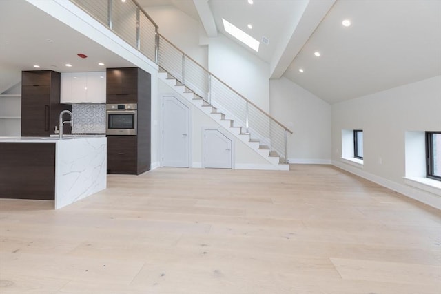 577 Massachusetts Ave Ph, Ph, Boston, MA 02118 - unfurnished living room with high vaulted ceiling, baseboards, stairway, light wood finished floors, and a skylight