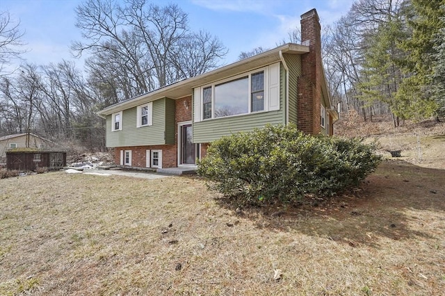 split foyer home featuring brick siding, a chimney, and a front lawn