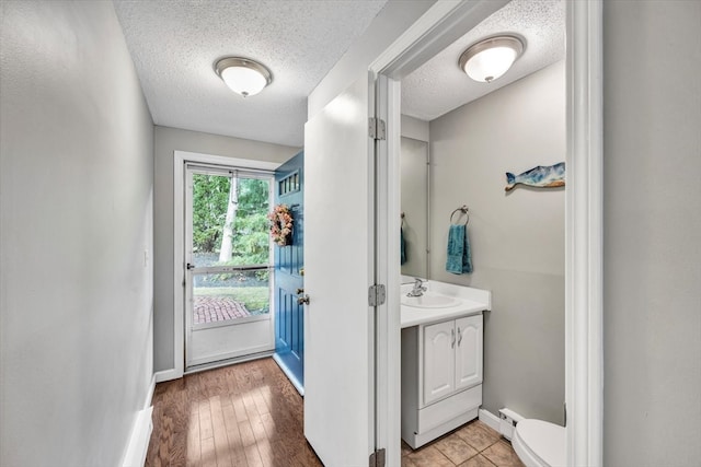 entryway with light wood-type flooring, a textured ceiling, sink, and a baseboard heating unit