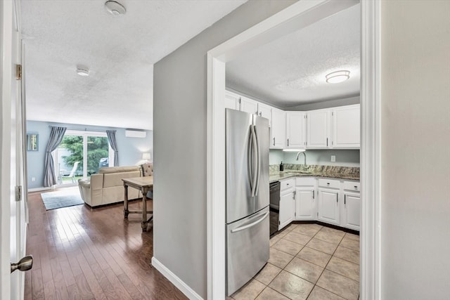 kitchen with stainless steel fridge, white cabinetry, light wood-type flooring, a textured ceiling, and sink