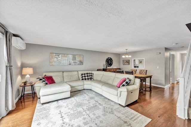 living room featuring an inviting chandelier, an AC wall unit, a textured ceiling, and hardwood / wood-style flooring