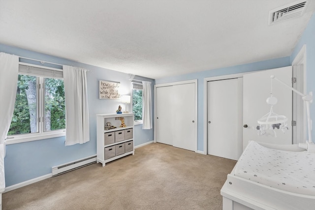 bedroom featuring a textured ceiling, a baseboard radiator, two closets, and carpet