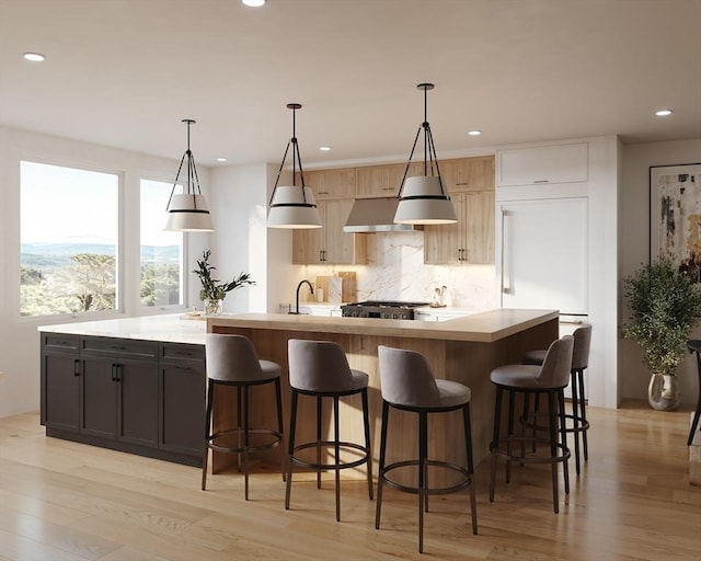 kitchen featuring light hardwood / wood-style flooring, backsplash, decorative light fixtures, light brown cabinetry, and a center island with sink