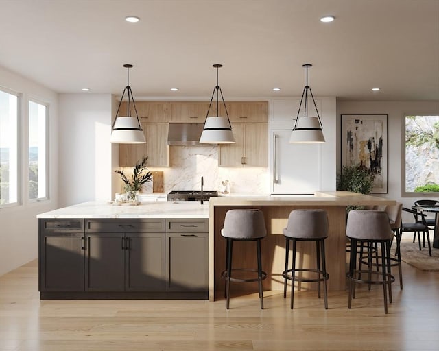 kitchen featuring light brown cabinets, a kitchen island with sink, light hardwood / wood-style flooring, light stone countertops, and decorative light fixtures