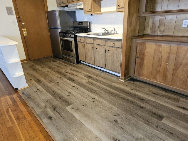 kitchen with a sink, stainless steel appliances, wood finished floors, and under cabinet range hood